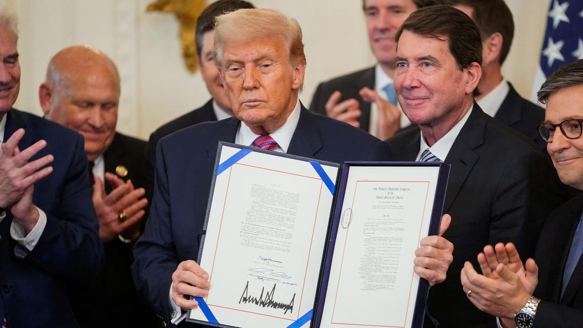 Donald Trump holding a signed law document surrounded by applauding officials during a signing ceremony.